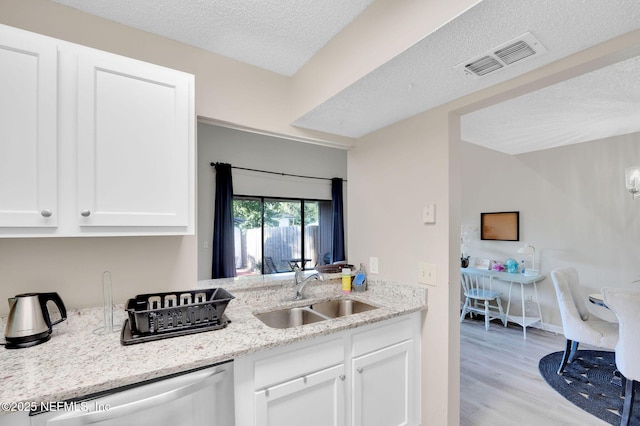 kitchen featuring light wood-type flooring, light stone counters, sink, dishwasher, and white cabinetry