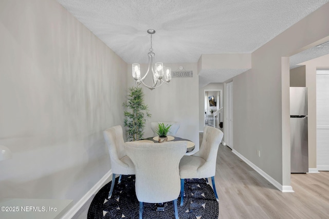 dining space featuring a textured ceiling, light hardwood / wood-style flooring, and an inviting chandelier