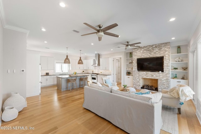 living room with ceiling fan, crown molding, light hardwood / wood-style flooring, built in features, and a fireplace