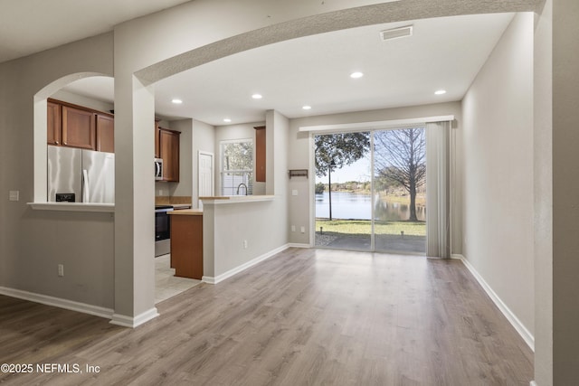 kitchen featuring light hardwood / wood-style floors, a water view, a healthy amount of sunlight, and appliances with stainless steel finishes