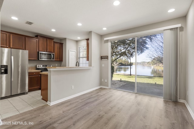 kitchen featuring kitchen peninsula, light hardwood / wood-style flooring, a water view, and stainless steel appliances