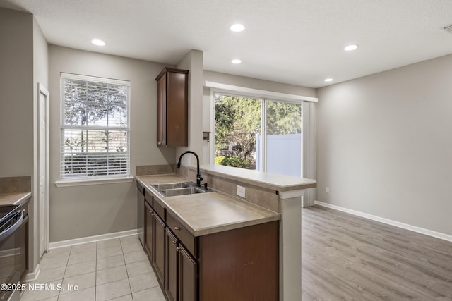 kitchen with sink, kitchen peninsula, a textured ceiling, dark brown cabinets, and range