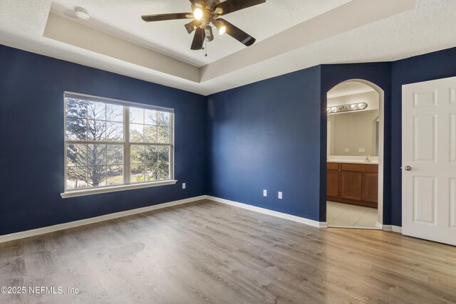 unfurnished room with a tray ceiling, ceiling fan, and light hardwood / wood-style flooring