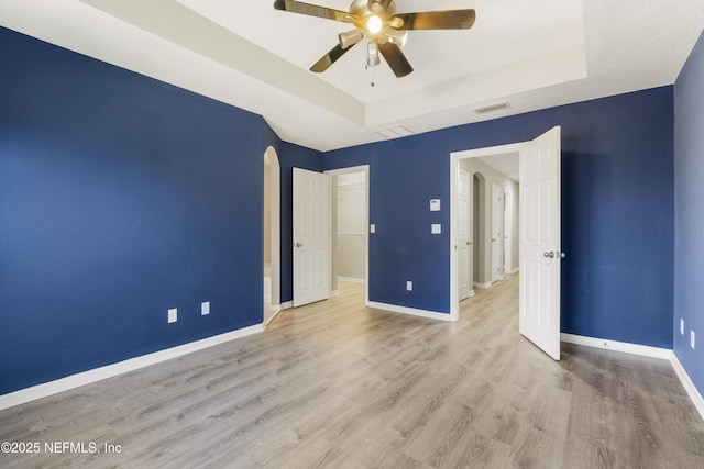 unfurnished bedroom featuring ceiling fan, a raised ceiling, and light wood-type flooring