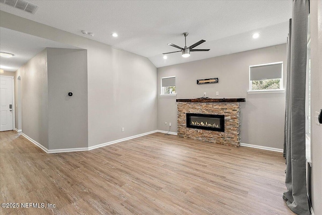 unfurnished living room with ceiling fan, a stone fireplace, light hardwood / wood-style floors, vaulted ceiling, and a textured ceiling