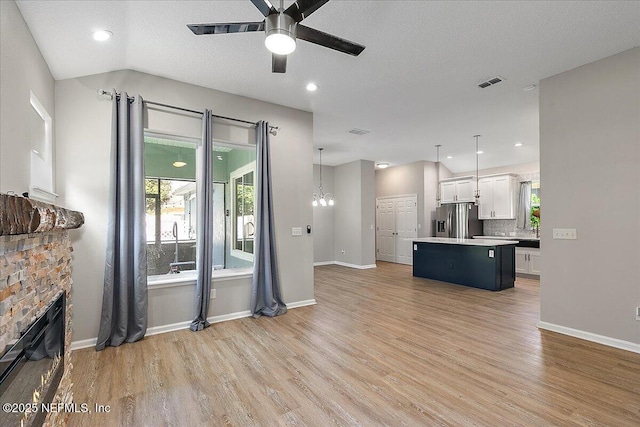 living room featuring light wood-type flooring, ceiling fan with notable chandelier, a textured ceiling, a stone fireplace, and lofted ceiling