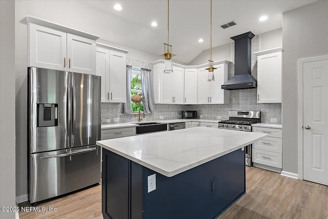 kitchen featuring wall chimney exhaust hood, stainless steel appliances, white cabinets, a kitchen island, and hanging light fixtures