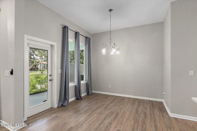 unfurnished dining area with wood-type flooring and an inviting chandelier