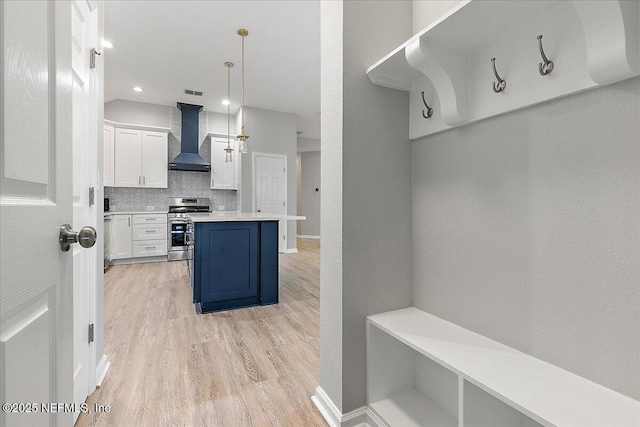 kitchen featuring a kitchen breakfast bar, wall chimney exhaust hood, stainless steel stove, white cabinetry, and hanging light fixtures