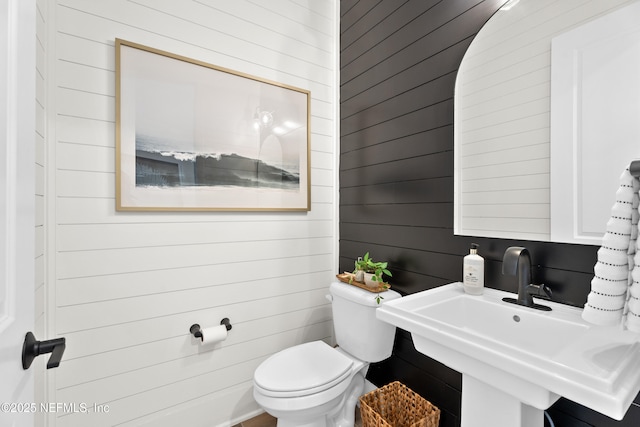 bathroom with toilet, sink, and wooden walls