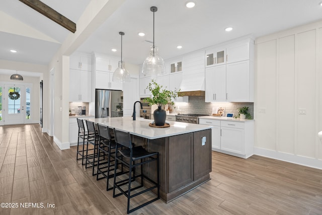 kitchen featuring white cabinetry, stainless steel fridge, a center island with sink, and custom exhaust hood