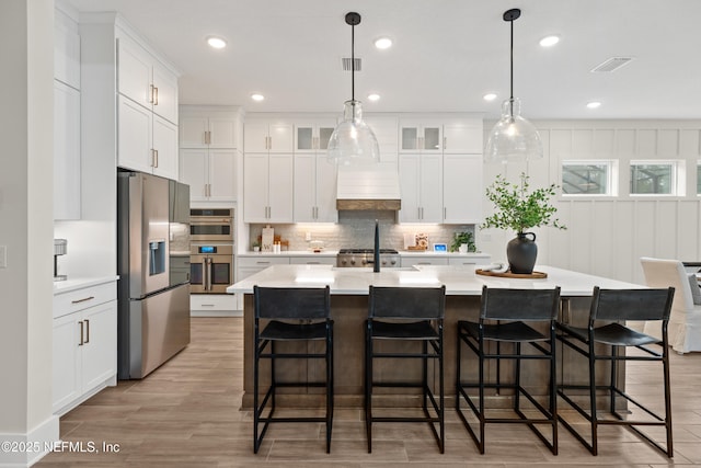 kitchen with a center island with sink, white cabinetry, hanging light fixtures, appliances with stainless steel finishes, and a kitchen breakfast bar