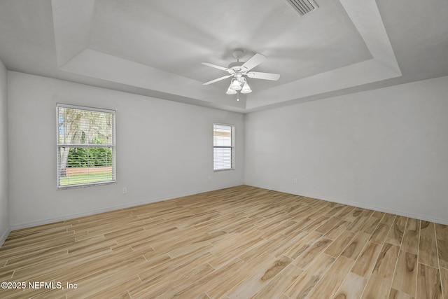 unfurnished room with a tray ceiling, a wealth of natural light, and light wood-type flooring