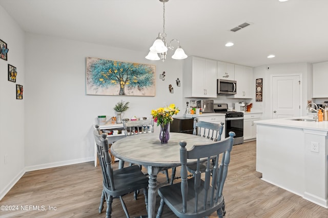 dining area with a notable chandelier, sink, and light hardwood / wood-style flooring