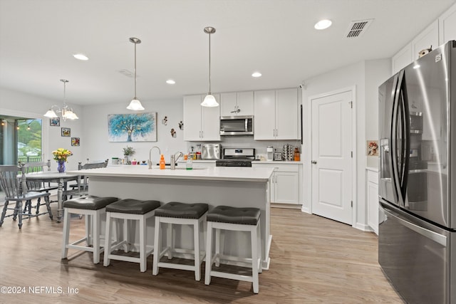 kitchen with pendant lighting, stainless steel appliances, white cabinetry, and an island with sink