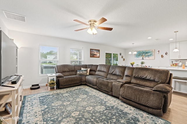 living room featuring ceiling fan with notable chandelier and light hardwood / wood-style floors