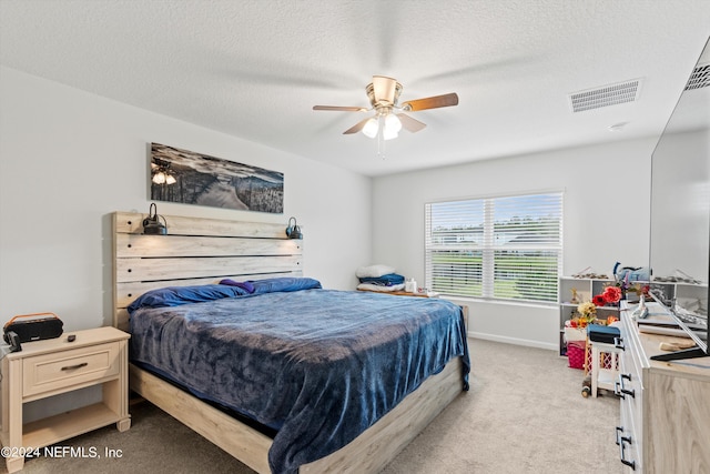 bedroom featuring a textured ceiling, light colored carpet, and ceiling fan