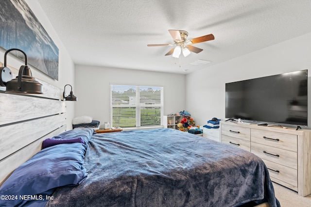 bedroom with ceiling fan, light colored carpet, and a textured ceiling