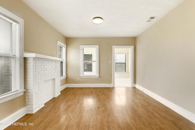 unfurnished room featuring a healthy amount of sunlight, light wood-type flooring, and a fireplace