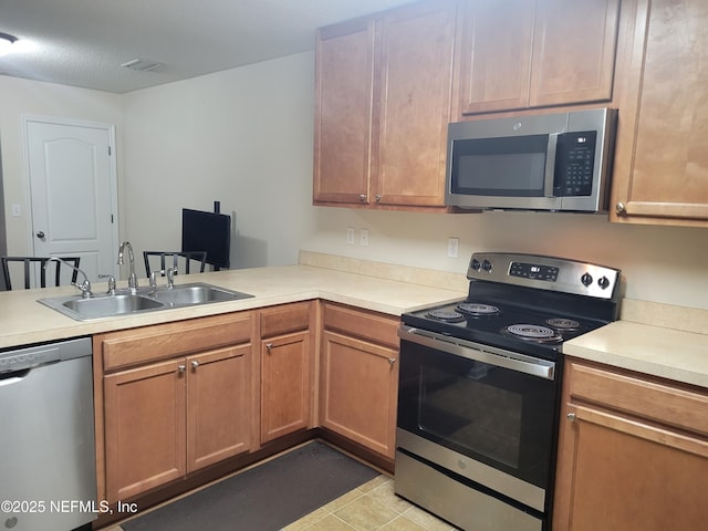 kitchen featuring appliances with stainless steel finishes, sink, light tile patterned floors, and kitchen peninsula