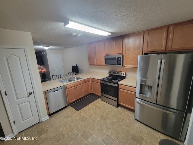 kitchen with appliances with stainless steel finishes, kitchen peninsula, sink, and a textured ceiling