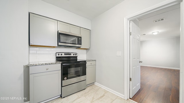 kitchen featuring decorative backsplash, light stone counters, gray cabinets, and stainless steel appliances