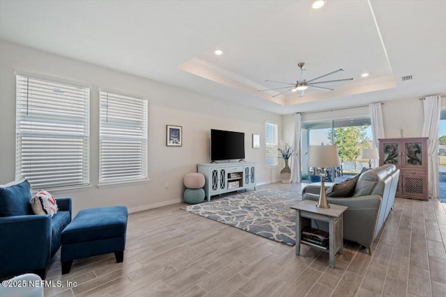 living room with ceiling fan, a tray ceiling, and light hardwood / wood-style floors