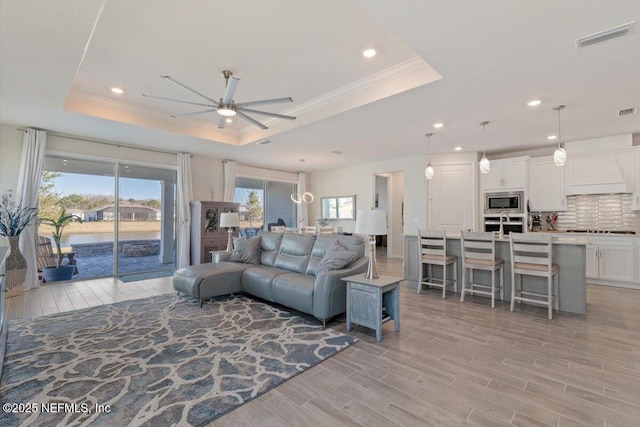 living room with light wood-type flooring, a tray ceiling, and a healthy amount of sunlight