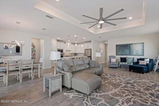 living room featuring ornamental molding, a raised ceiling, and ceiling fan with notable chandelier