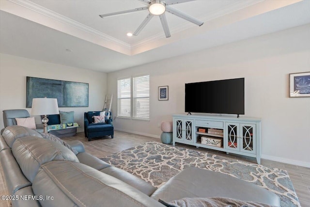 living room with ceiling fan, light hardwood / wood-style flooring, a raised ceiling, and crown molding