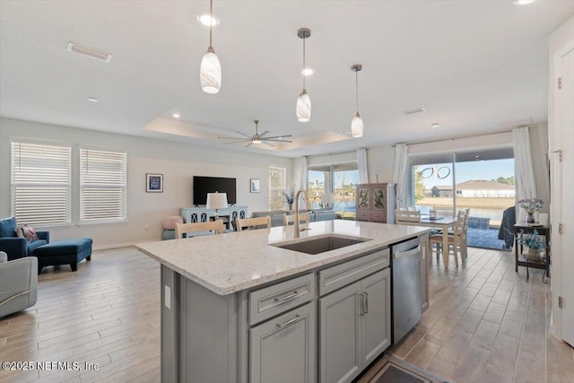 kitchen with dishwasher, an island with sink, a raised ceiling, ceiling fan, and sink