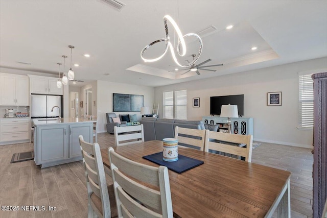 dining space with ceiling fan with notable chandelier, a tray ceiling, light hardwood / wood-style floors, and sink