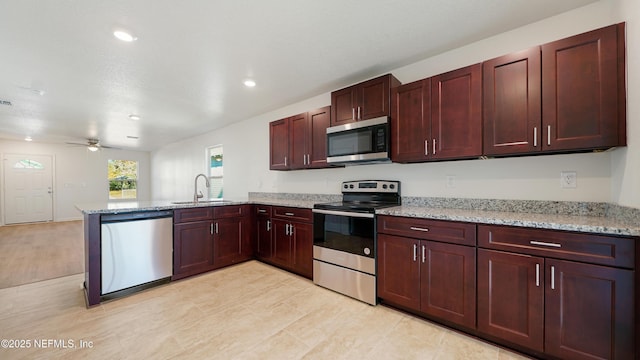 kitchen featuring ceiling fan, light stone counters, appliances with stainless steel finishes, and kitchen peninsula