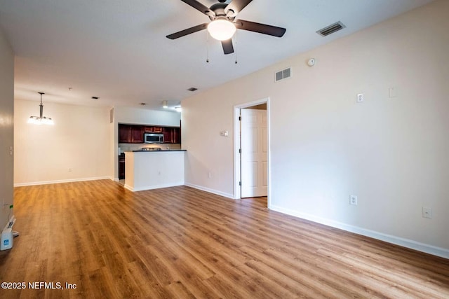 unfurnished living room featuring ceiling fan with notable chandelier and light hardwood / wood-style floors