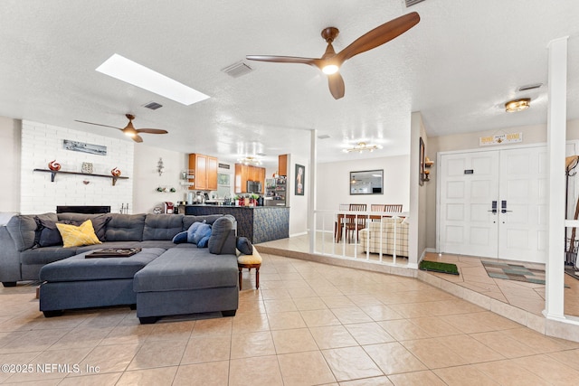 tiled living room featuring ceiling fan, a textured ceiling, and a skylight