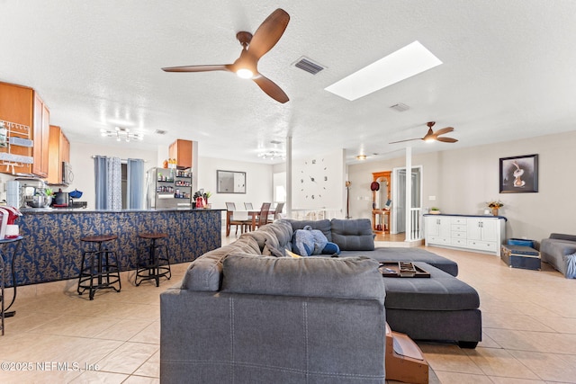 tiled living room with a textured ceiling, ceiling fan, and a skylight