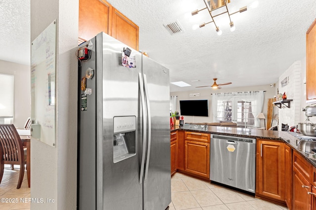 kitchen with light tile patterned floors, appliances with stainless steel finishes, dark stone countertops, a textured ceiling, and ceiling fan with notable chandelier