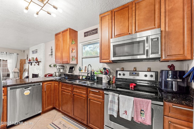 kitchen with a textured ceiling, stainless steel appliances, dark stone countertops, and sink