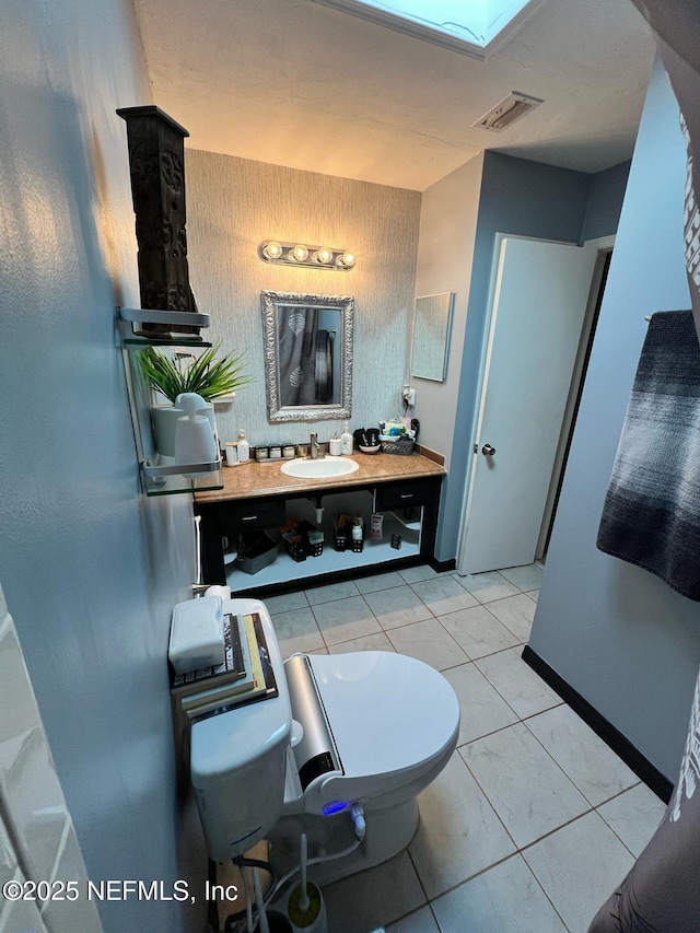 bathroom with toilet, a skylight, tile patterned flooring, and vanity