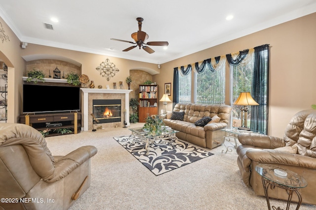 carpeted living room with crown molding, a tile fireplace, and ceiling fan