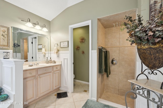 bathroom with a tile shower, lofted ceiling, tile patterned flooring, vanity, and toilet