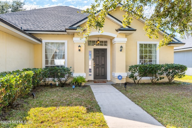 doorway to property featuring stucco siding, a shingled roof, and a yard