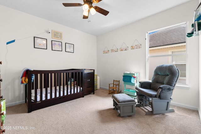 carpeted bedroom with a crib, baseboards, and a ceiling fan