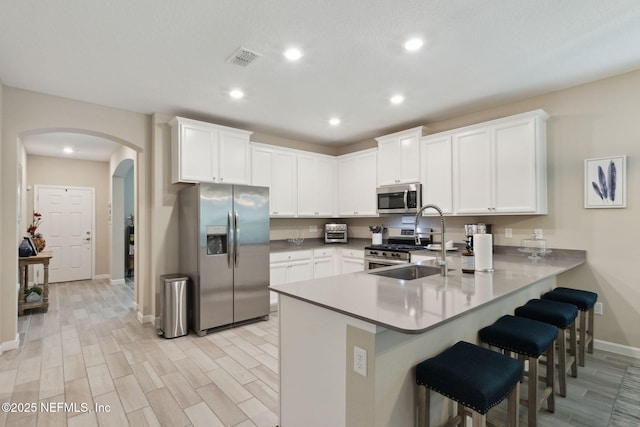 kitchen featuring a breakfast bar, stainless steel appliances, white cabinets, a sink, and a peninsula