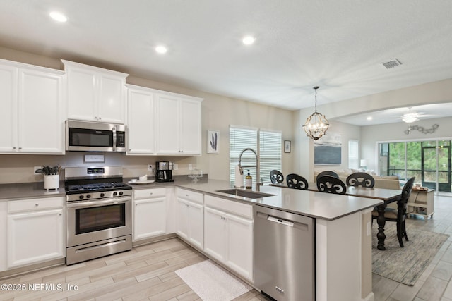 kitchen featuring decorative light fixtures, appliances with stainless steel finishes, white cabinets, a sink, and a peninsula