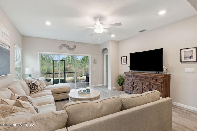 living area featuring arched walkways, ceiling fan, visible vents, baseboards, and light wood-type flooring