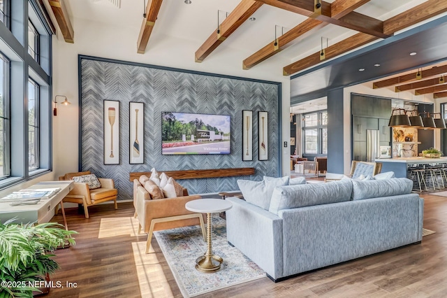 living room featuring an accent wall, wood finished floors, beam ceiling, and wallpapered walls