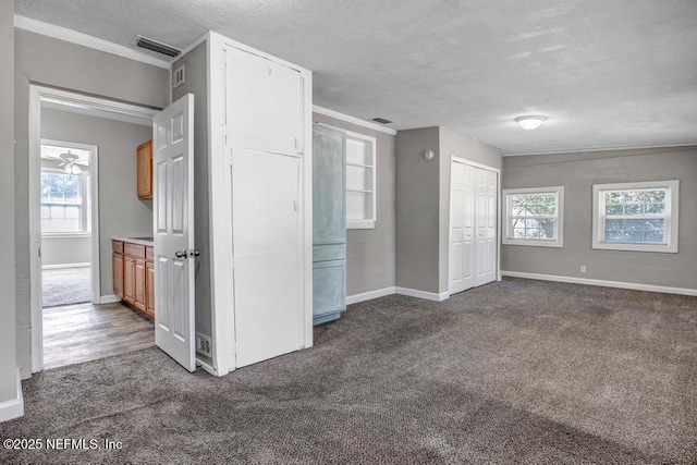 empty room with dark carpet, a textured ceiling, and ornamental molding