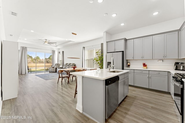 kitchen with stainless steel appliances, light hardwood / wood-style flooring, ceiling fan, and a center island with sink