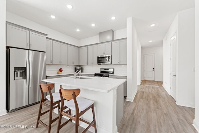 kitchen featuring a kitchen island with sink, sink, light hardwood / wood-style flooring, a kitchen bar, and stainless steel appliances